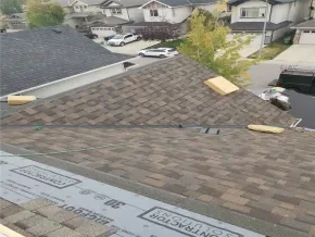 A sloped roof with shingles, a few boards, and construction materials visible