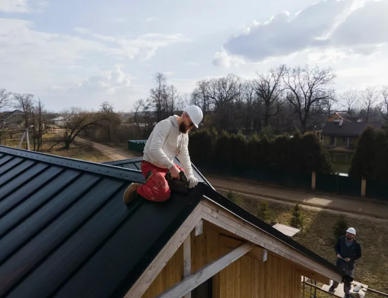 A worker installs materials on a sloped roof under a partly cloudy sky