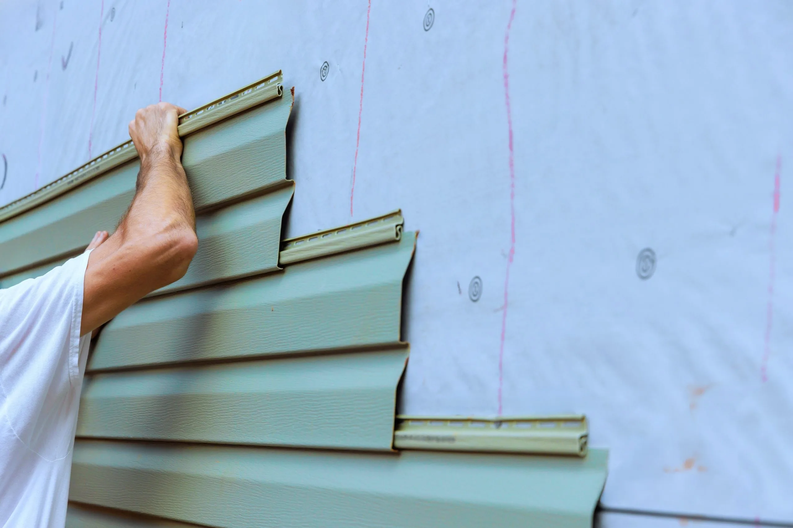 A person installs green siding against a prepared wall surface