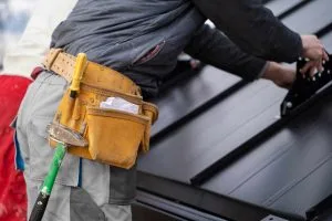Roofing Okotoks worker installs materials while wearing a tool belt